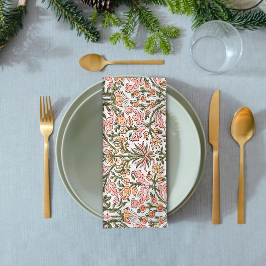 Set table with floral napkin, gold cutlery, and Christmas decorations.
