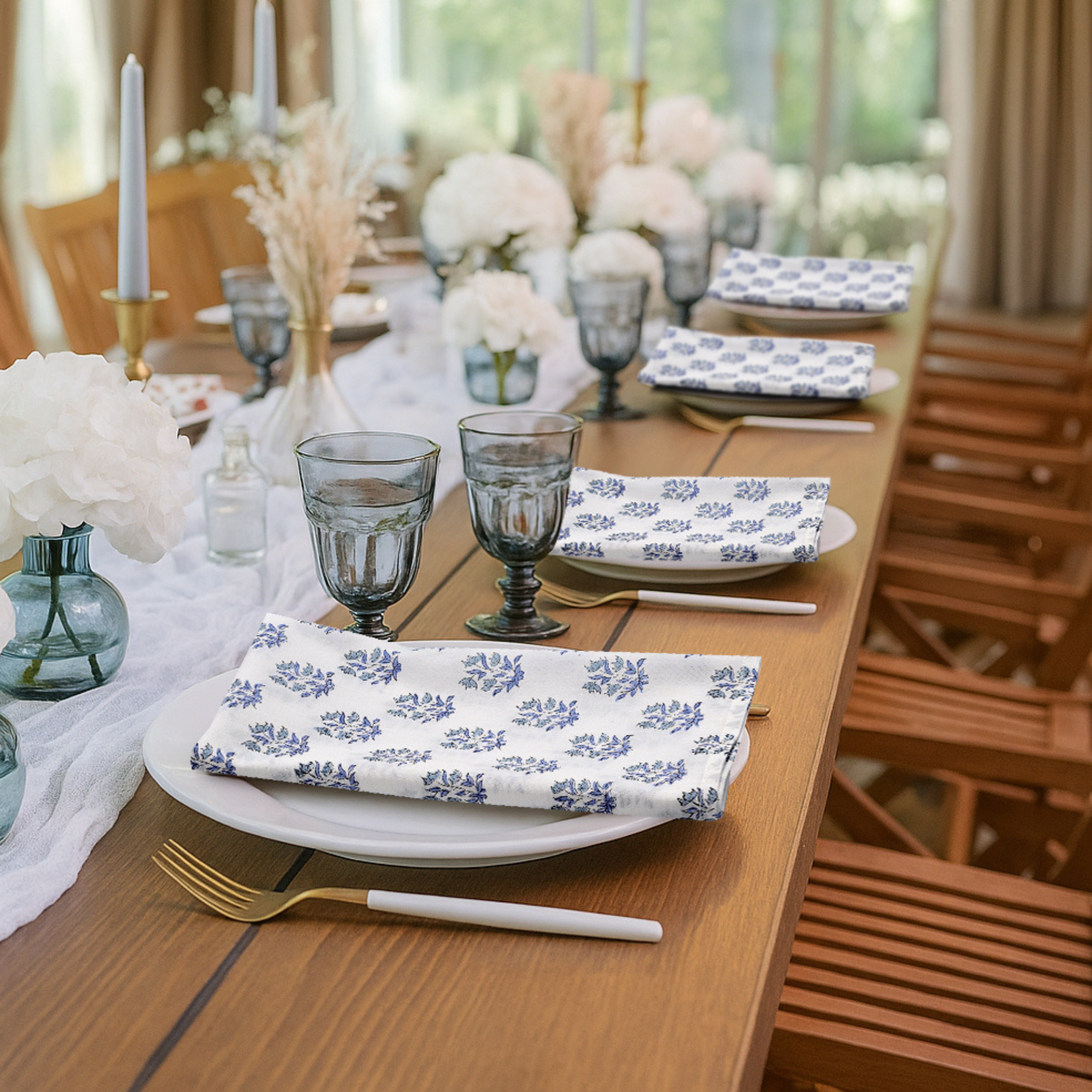 Dining table set with floral-patterned plates, glasses, and napkins in a bright room.
