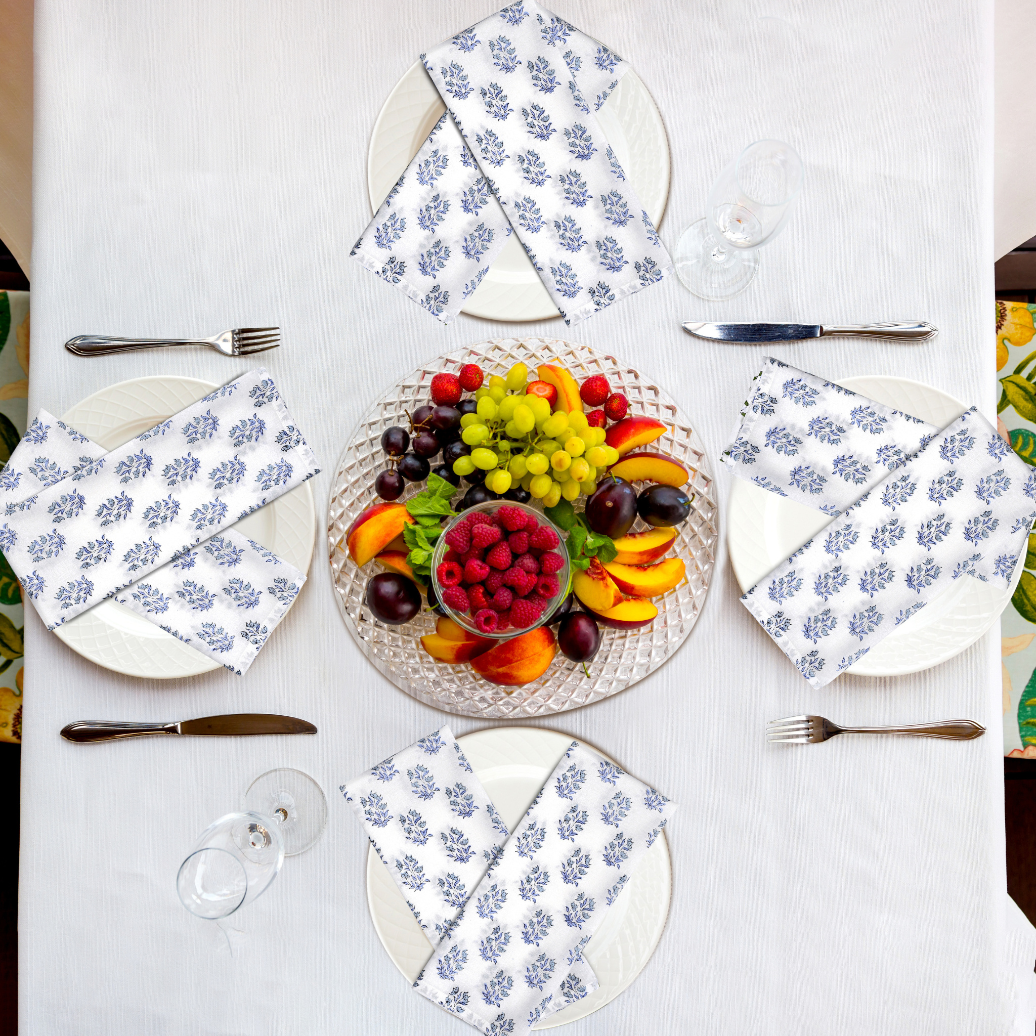 Table setting with fruit platter and floral napkins on a white tablecloth.