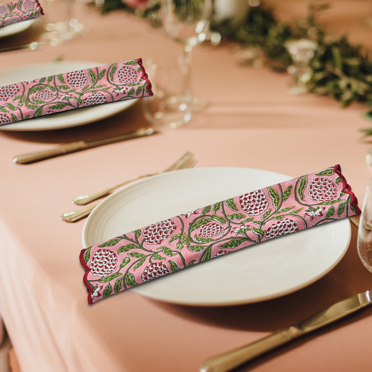 Table setting with pink and green patterned napkins on a peach-colored tablecloth.