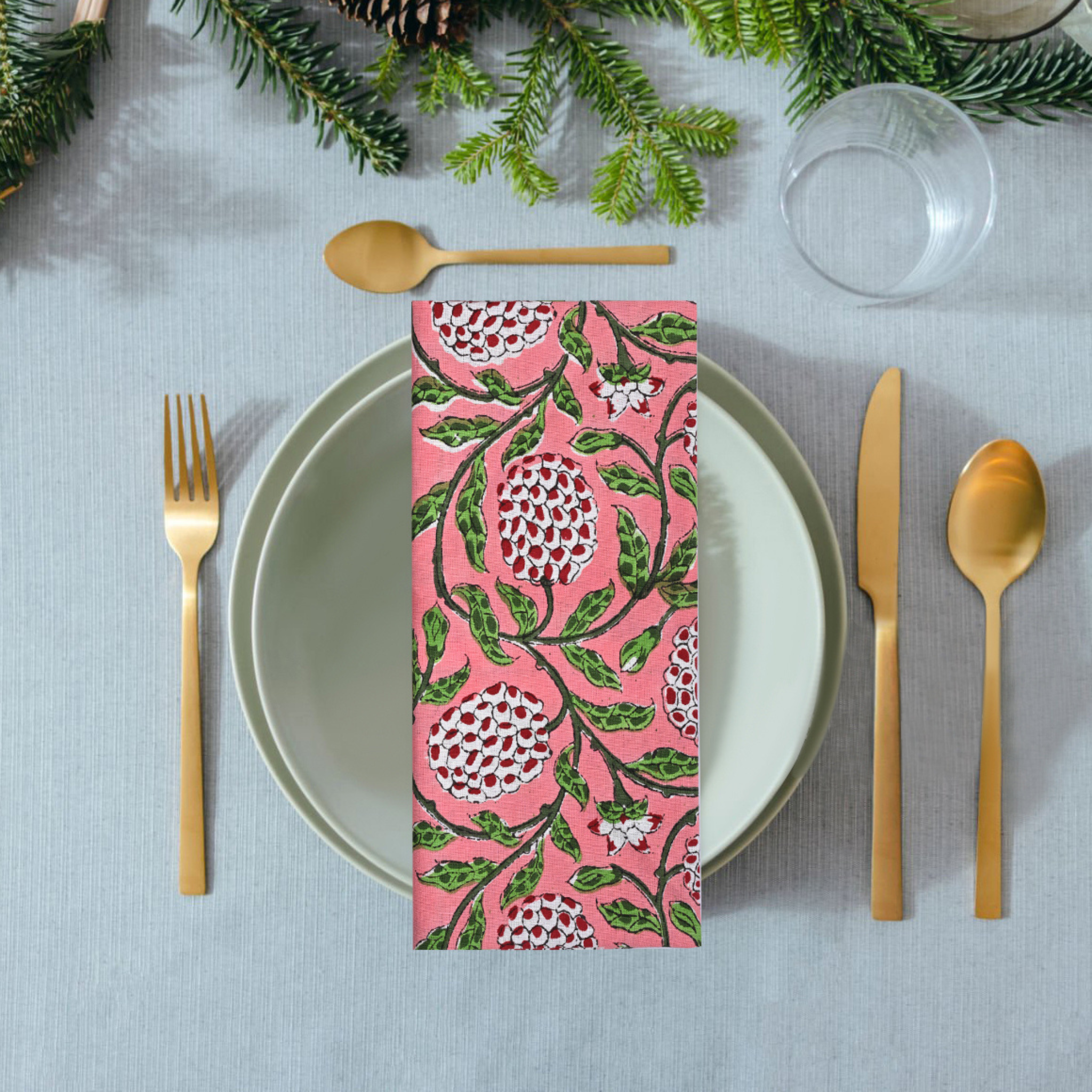 Napkin with pink floral design on a table setting with cutlery and greenery.