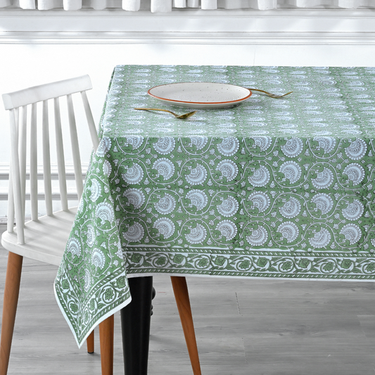Green patterned tablecloth on a dining table with a chair in a kitchen setting.