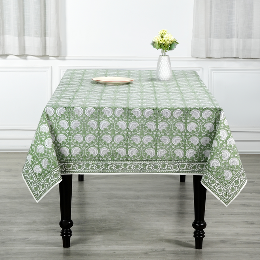 Green patterned tablecloth on a table with a vase of flowers in a room.