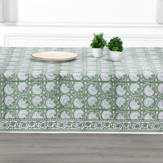 Green and white patterned tablecloth on a wooden table with plants and a plate.