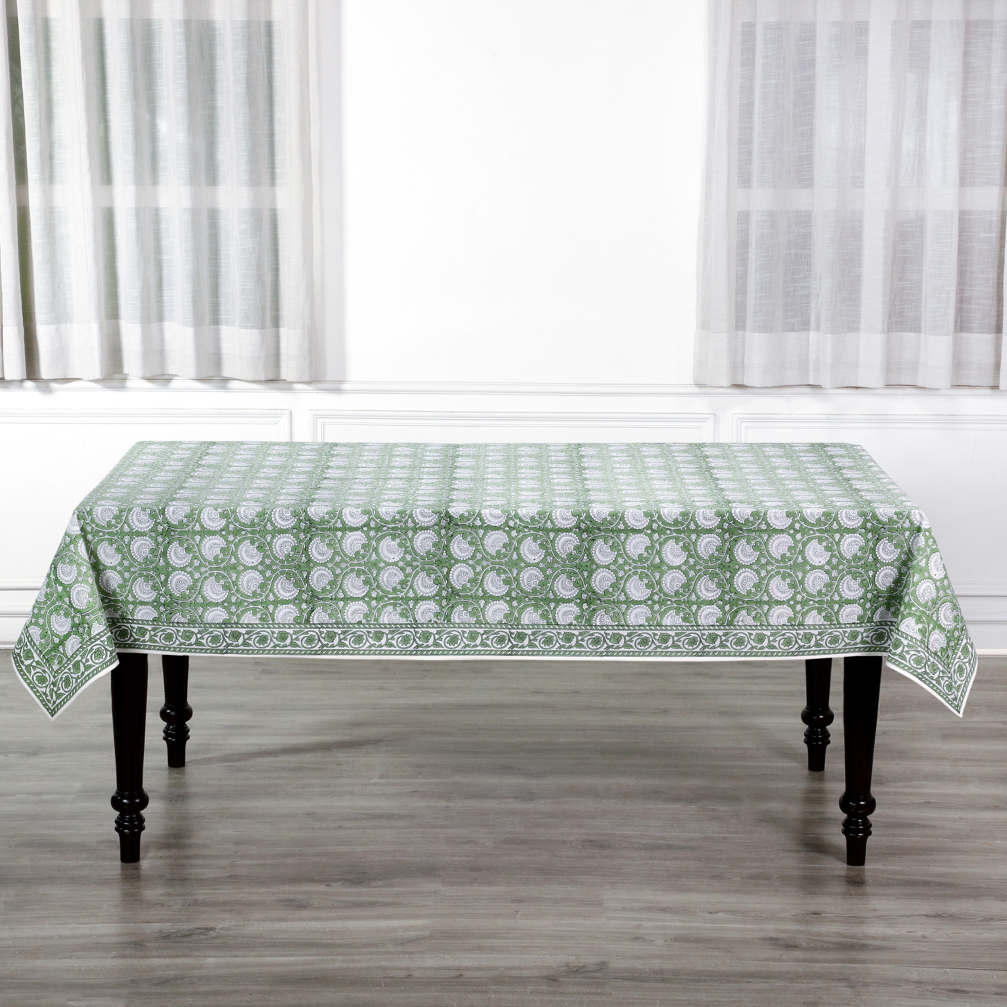 Tablecloth with green floral pattern on a wooden table in a room with white curtains.