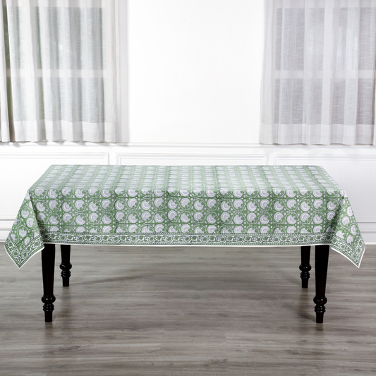 Tablecloth with green floral pattern on a wooden table in a room with white curtains.