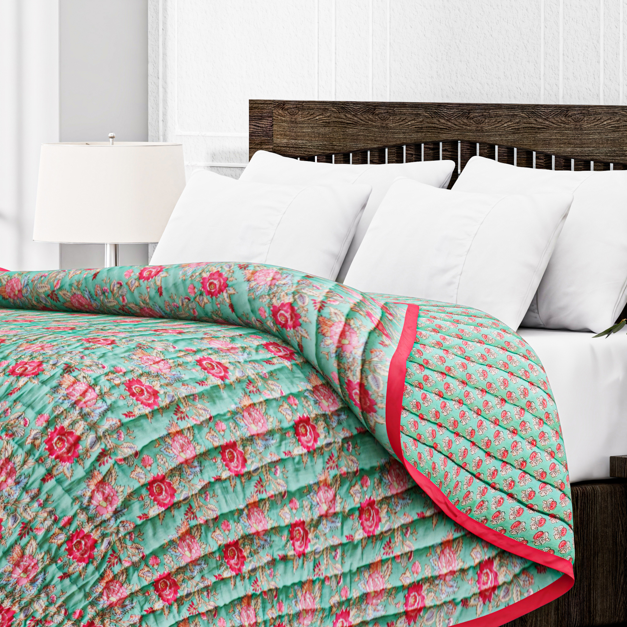 Floral quilt with pink roses on a bed with white pillows and wooden headboard.