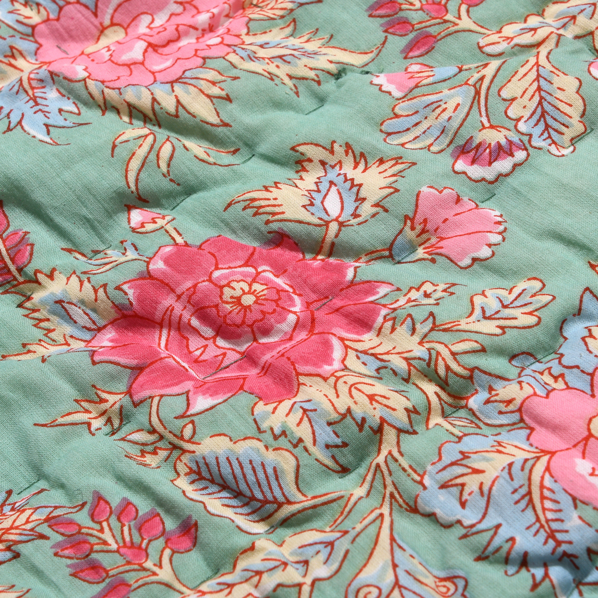 Close-up of a floral patterned fabric with pink and blue flowers on a green background.