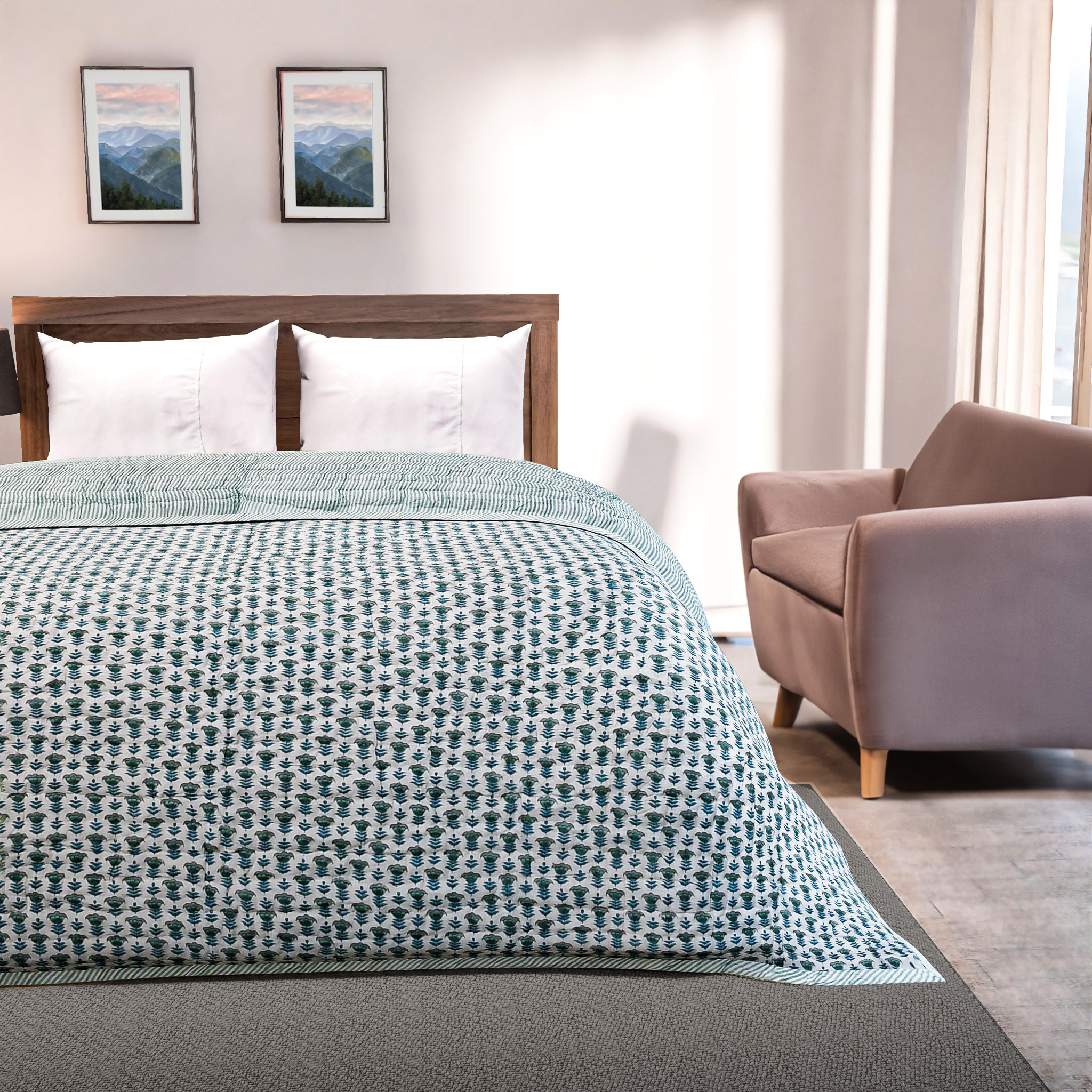 Bedroom with a bed covered in a green and white patterned comforter, a chair, and framed pictures on the wall.