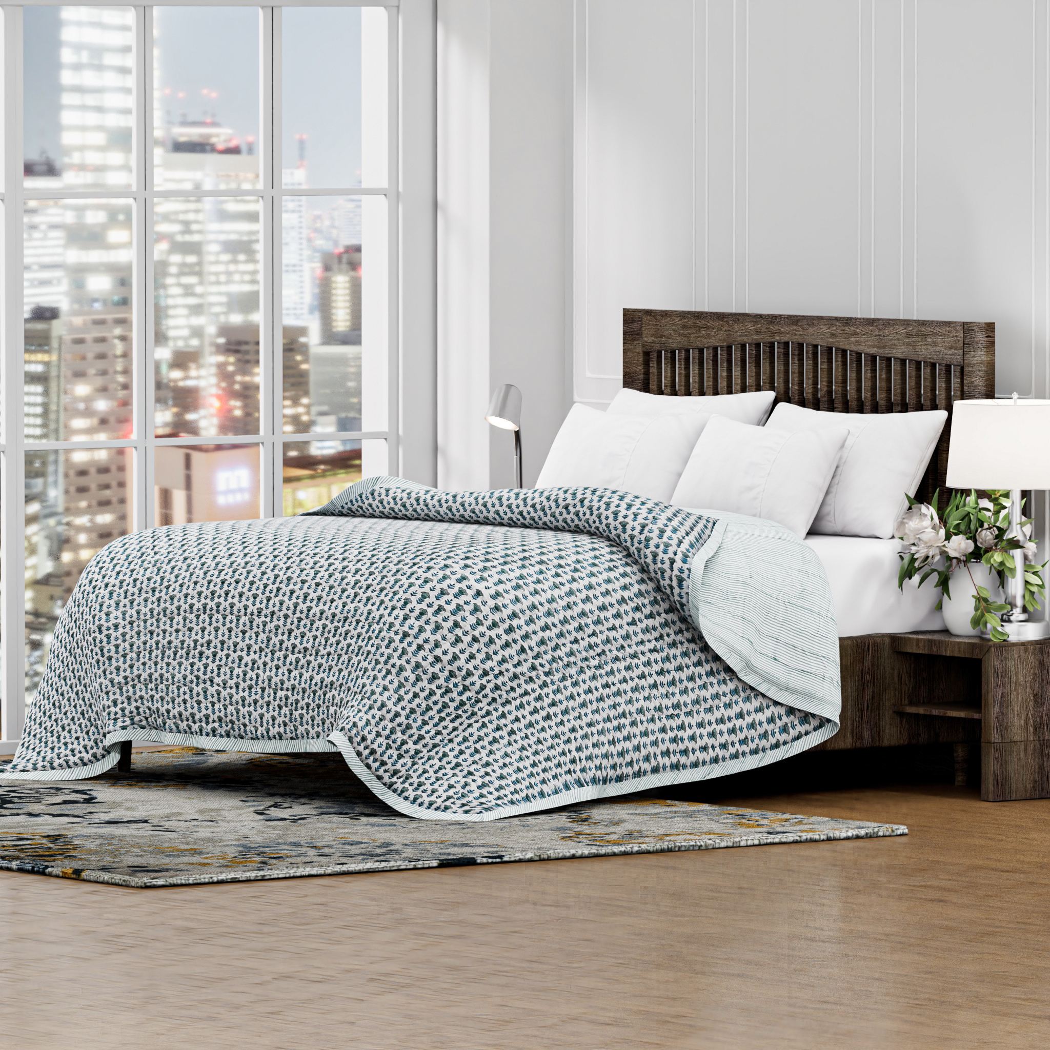 Bedroom with a large window view of a city skyline, featuring a bed with a textured gray blanket and white pillows.