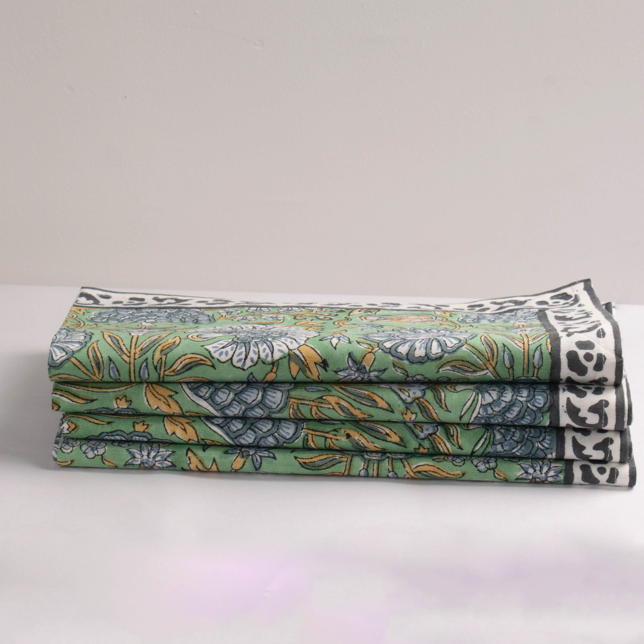 Stack of folded fabric with green floral pattern on a light gray background
