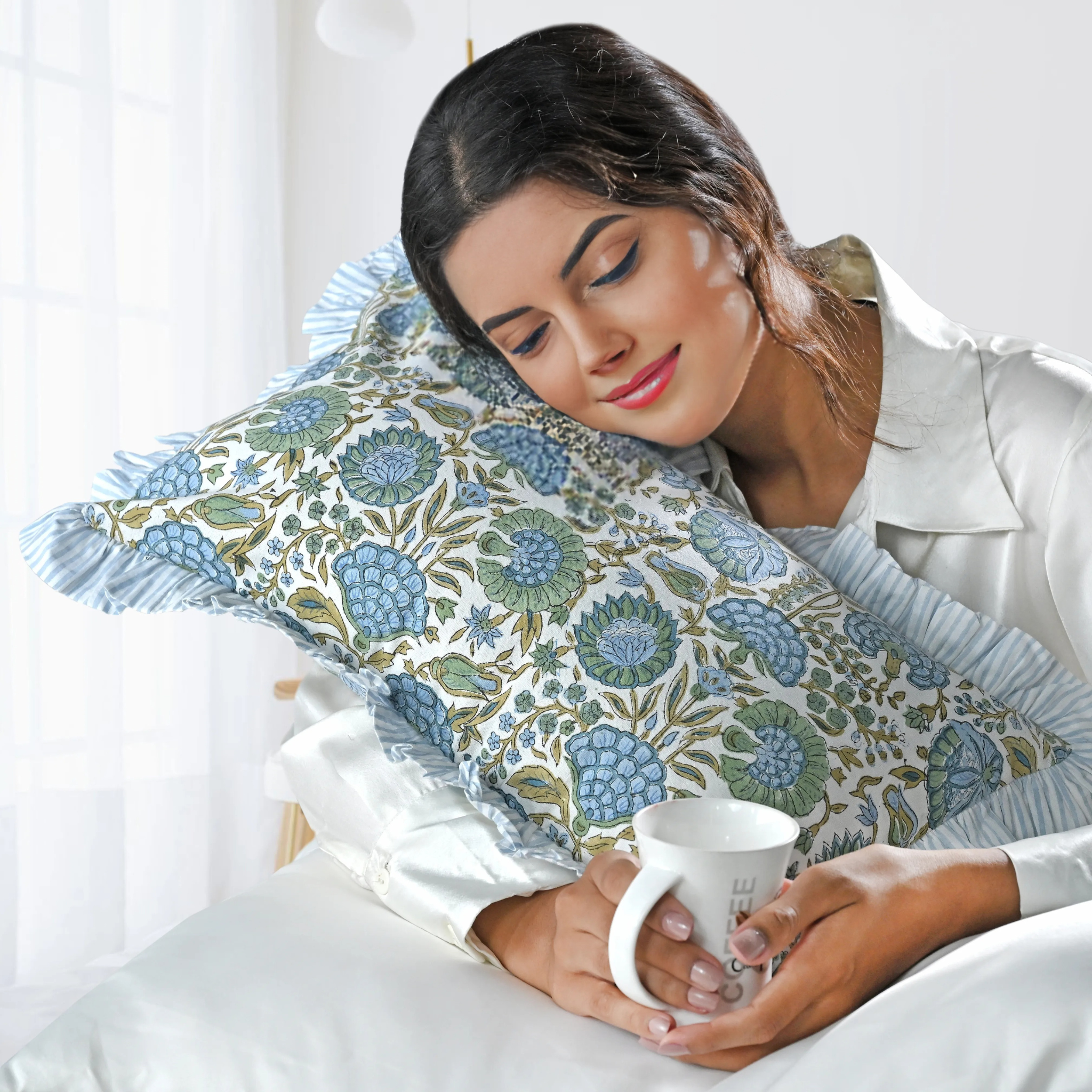 Woman holding a mug with a floral-patterned pillow behind her head on a white background