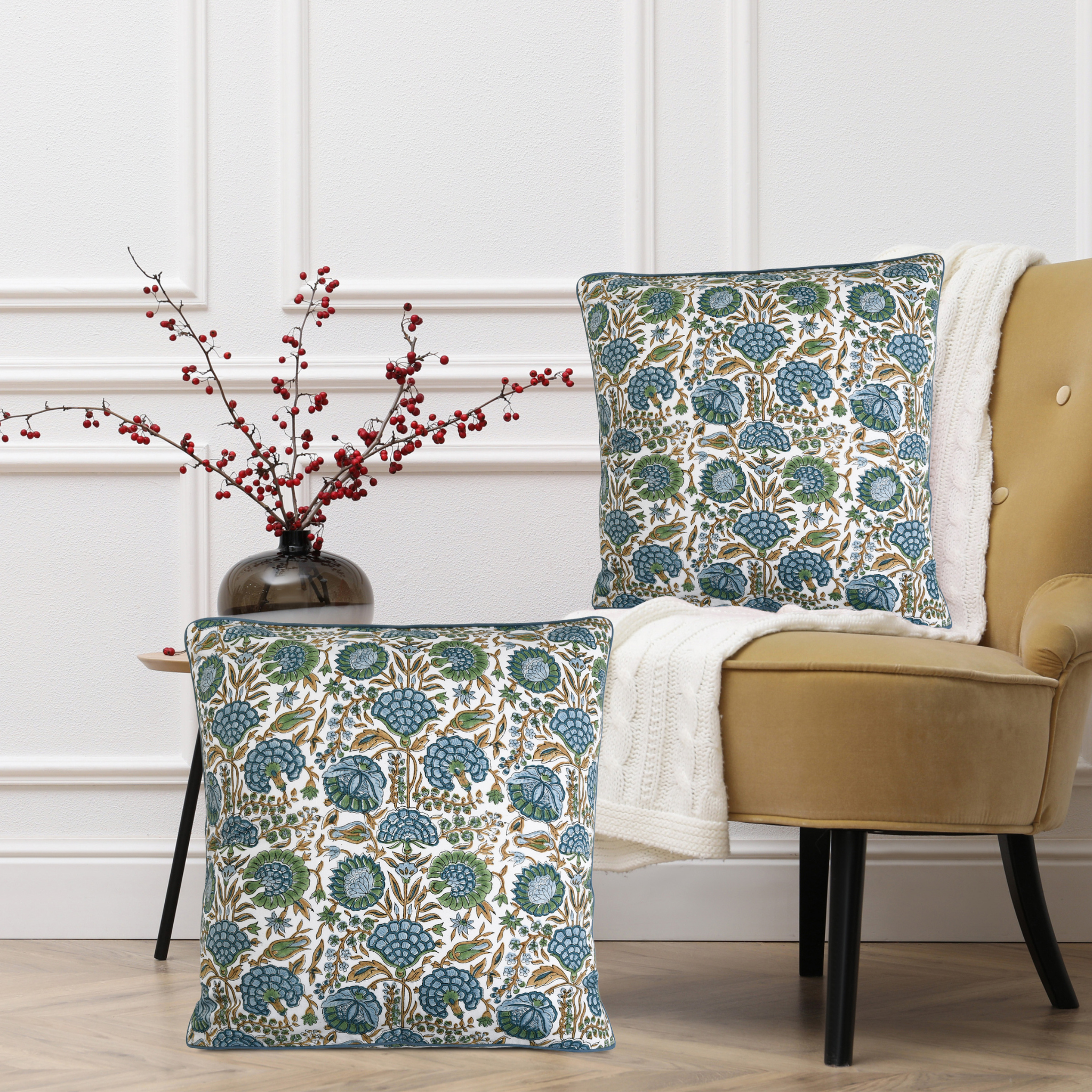 Floral patterned cushions on a chair with a vase of red berries on a side table.