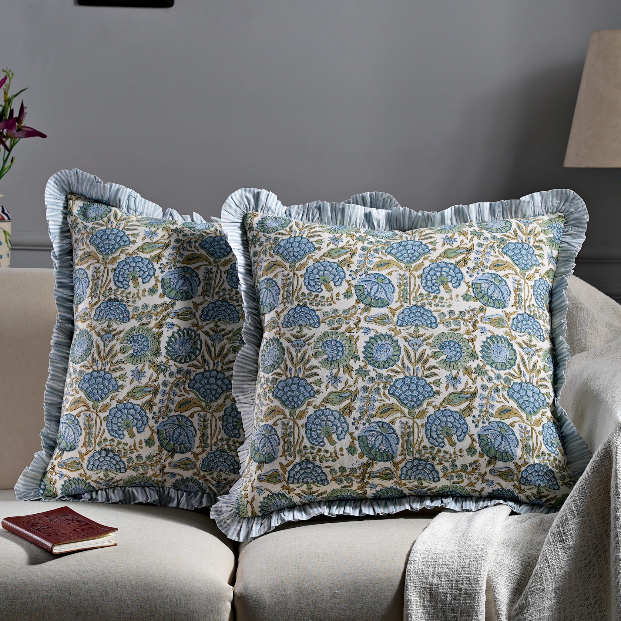 Floral patterned pillows with ruffled edges on a sofa against a gray wall.