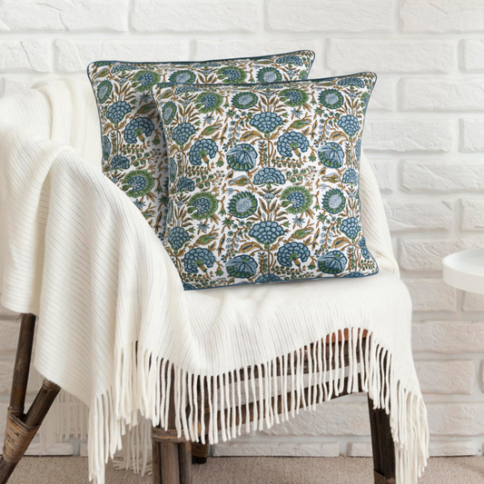 Decorative pillows with floral pattern on a white chair against a white brick wall.