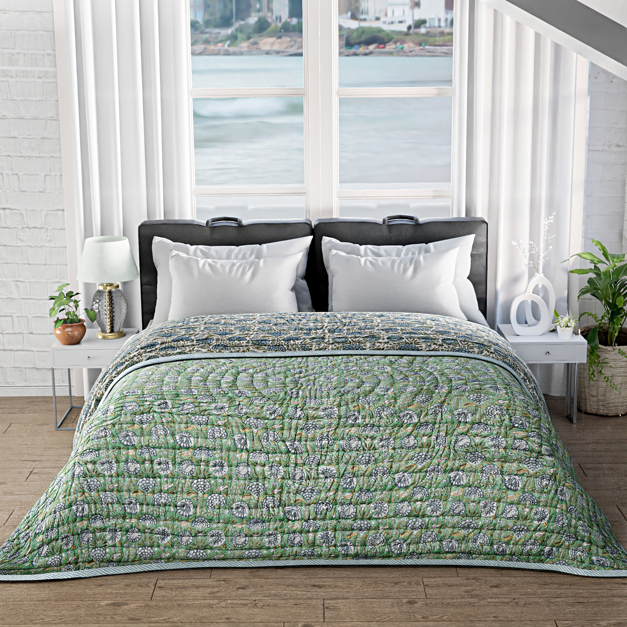 Bed with green floral quilt and white pillows in a room with large windows.
