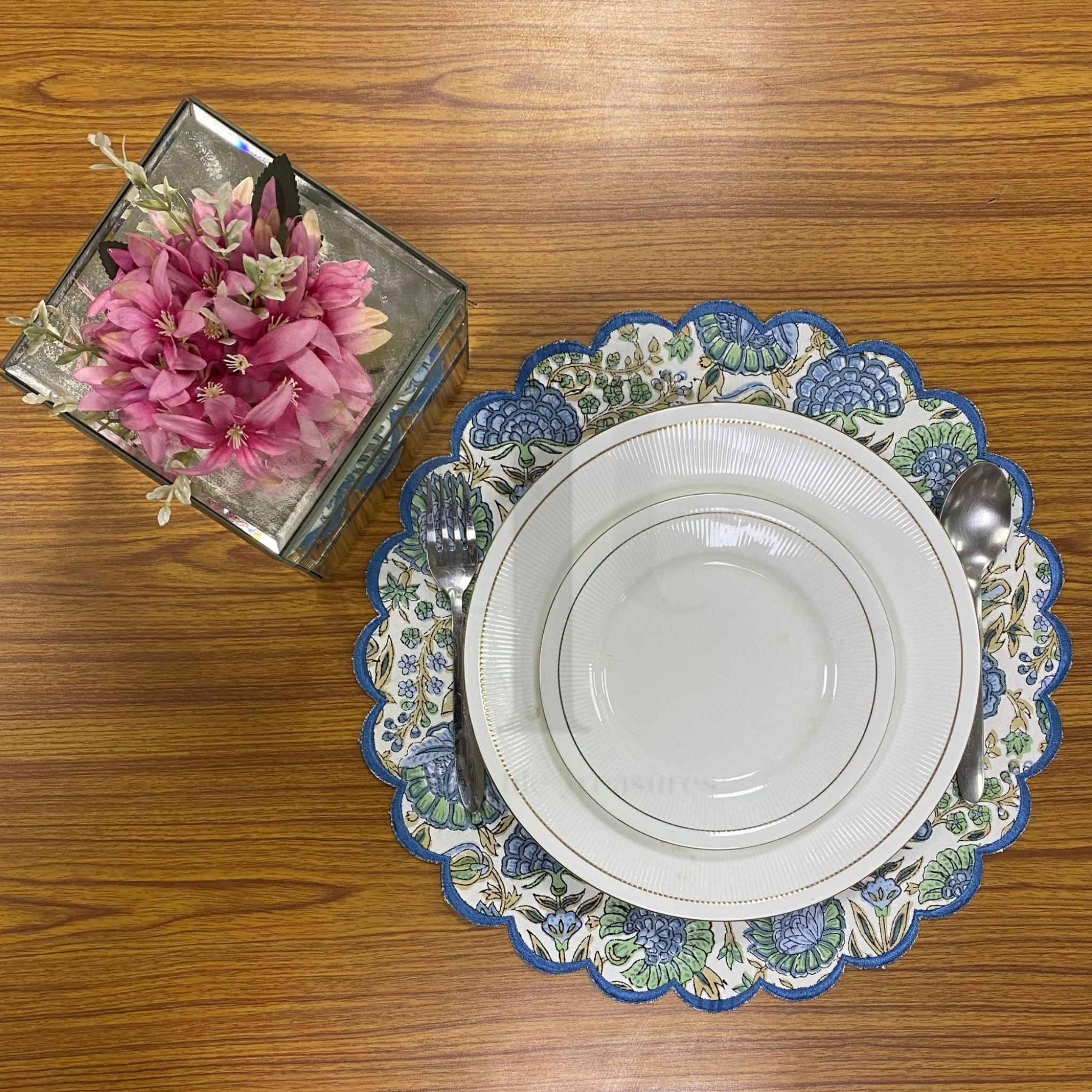 Decorative plate with floral design on a wooden table, next to a small box with pink flowers.