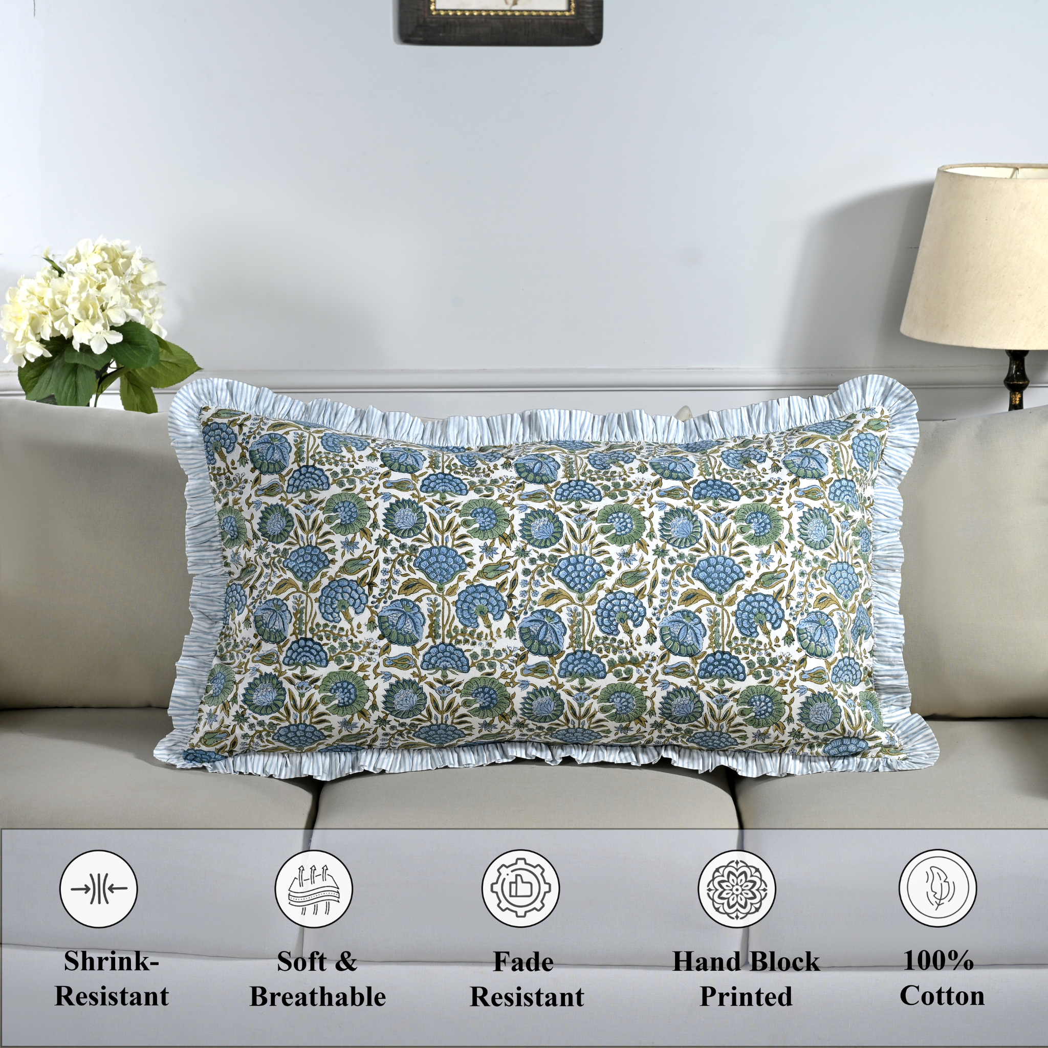 Cotton block print pillow cover placed on a bed with lamp and flowers in background.