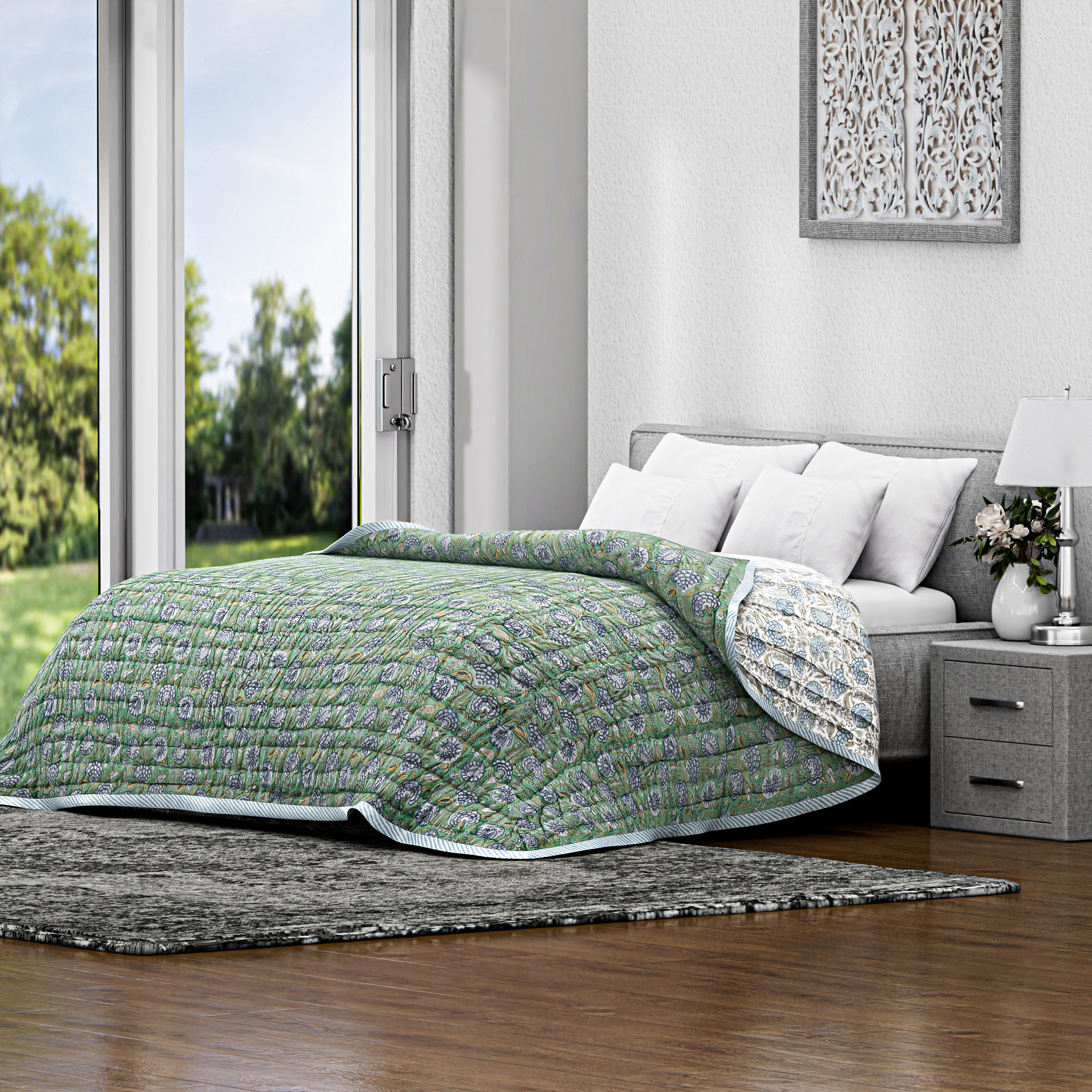 Bed with green quilt in a bright bedroom with large windows.
