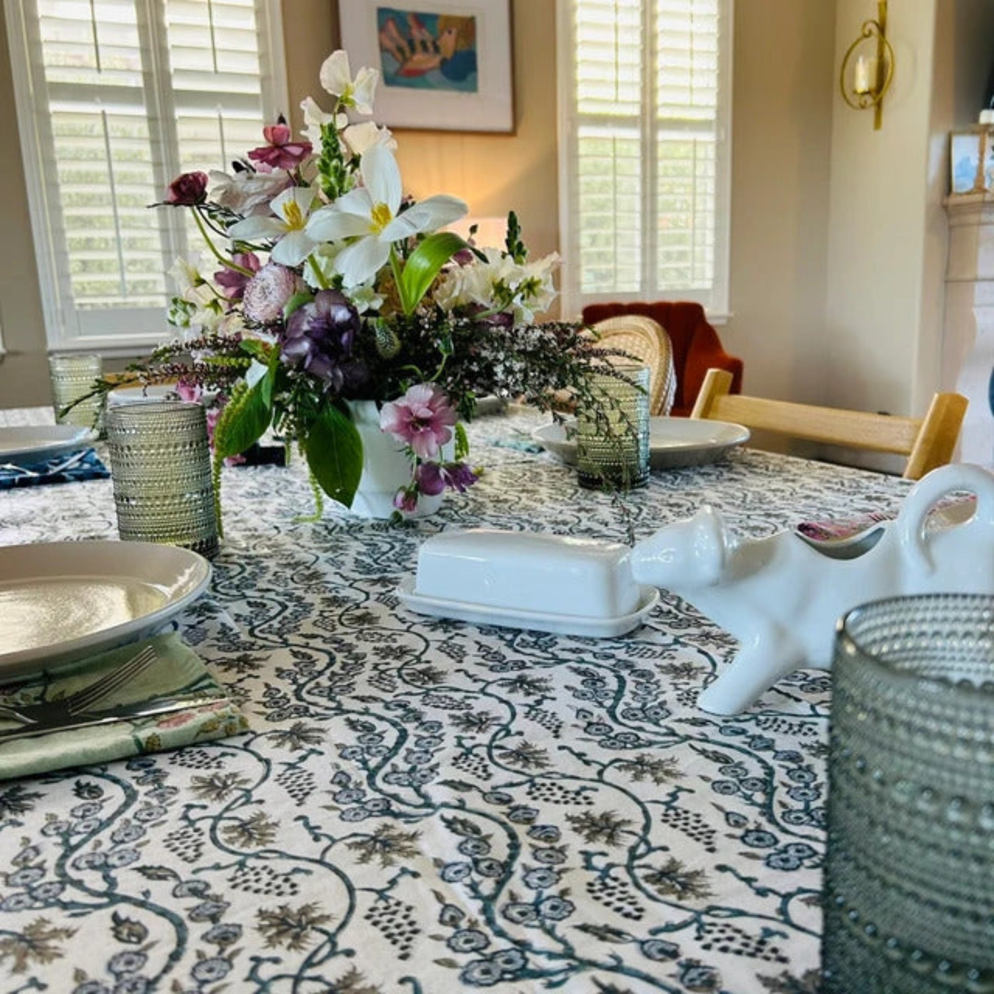 Dining table set with a floral centerpiece, plates, and decorative items in a well-lit room.
