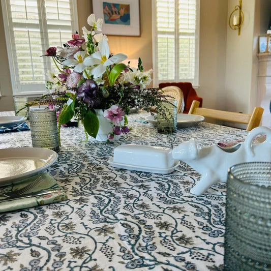 Dining table set with a floral centerpiece, plates, and decorative items in a well-lit room.