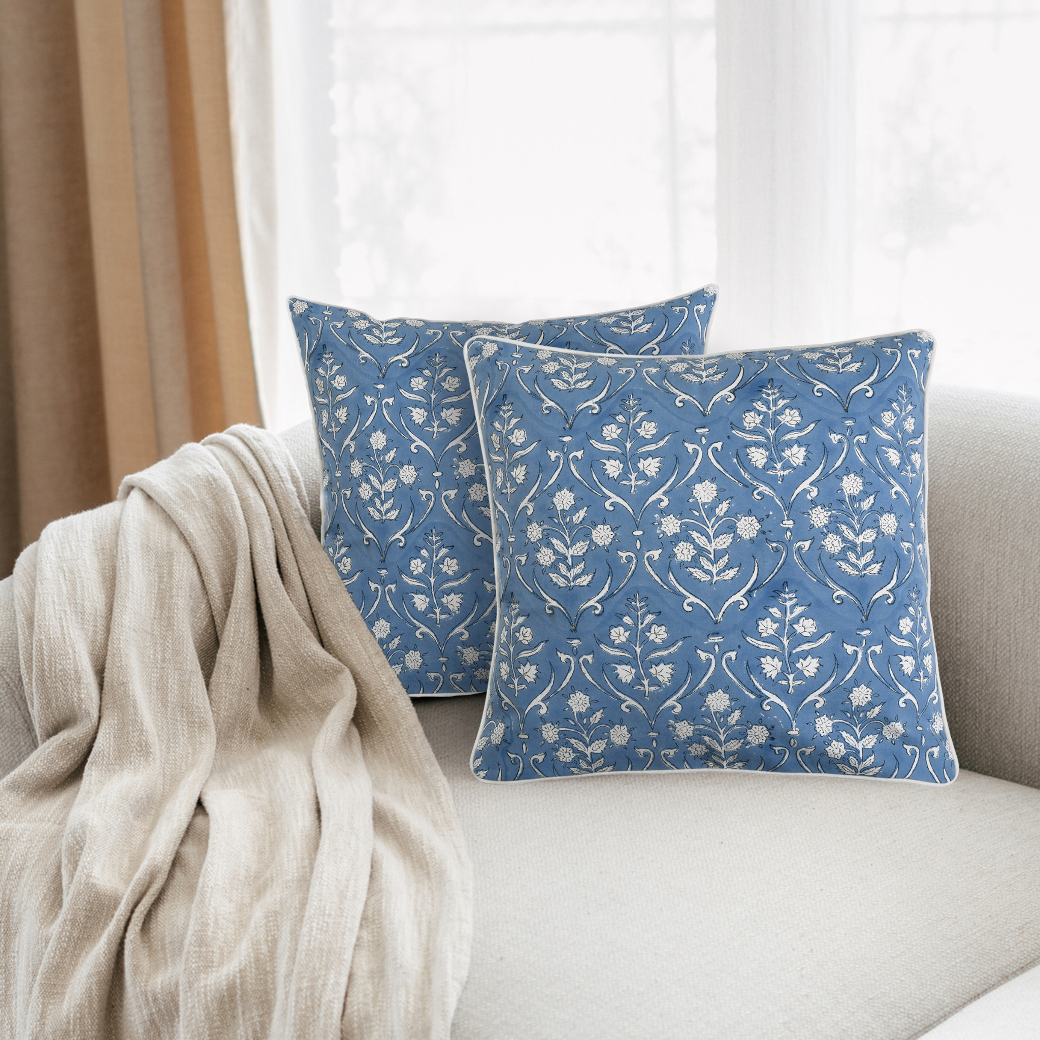 Blue patterned pillows on a white sofa with beige blanket