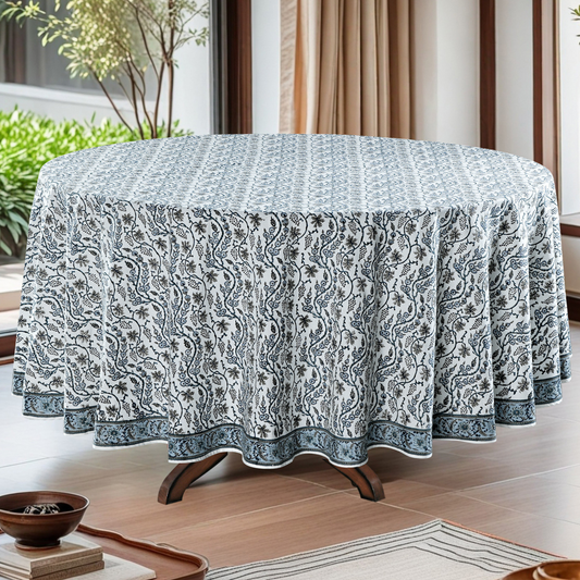 Round table with a patterned tablecloth in a room with plants and curtains.