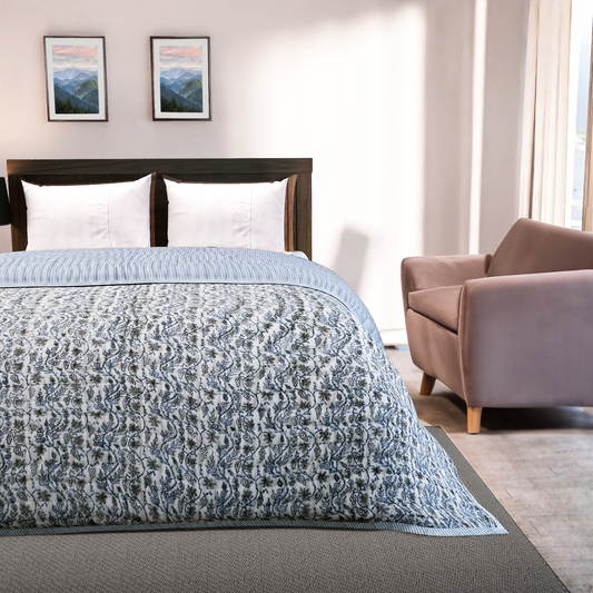Bedroom with a bed covered in a blue patterned comforter, a chair, and framed pictures on the wall.