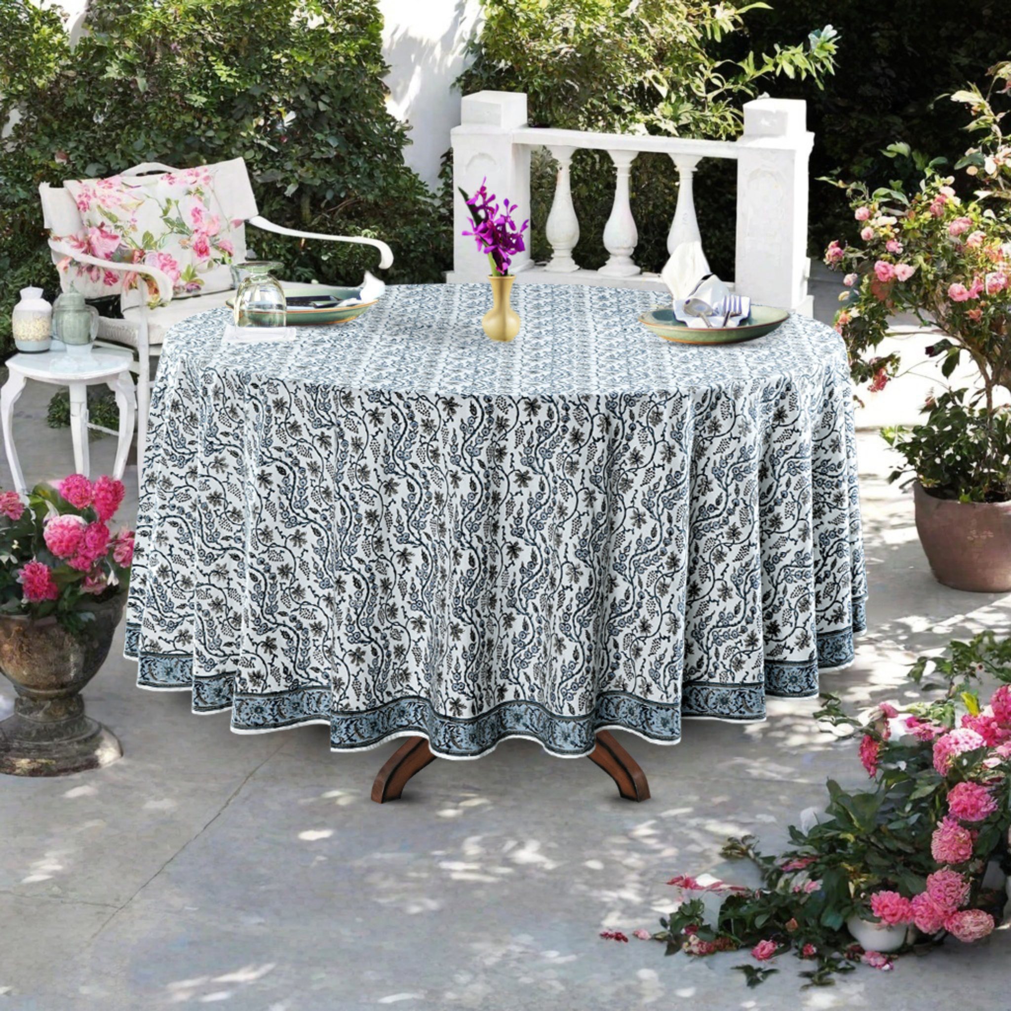 Outdoor table setting with a patterned tablecloth, chairs, and floral arrangements.