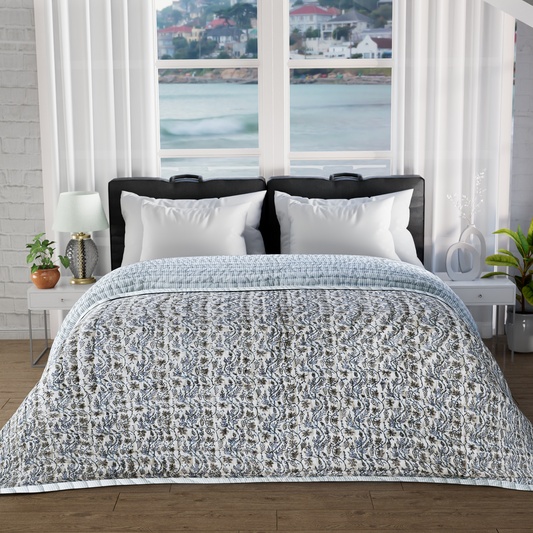 Bed with patterned quilt and white pillows in a room with large windows showing a scenic view.