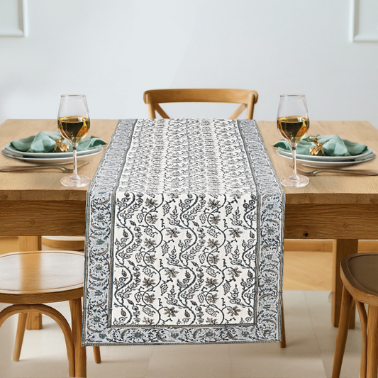 Dining table set with a patterned table runner, glasses, and plates.