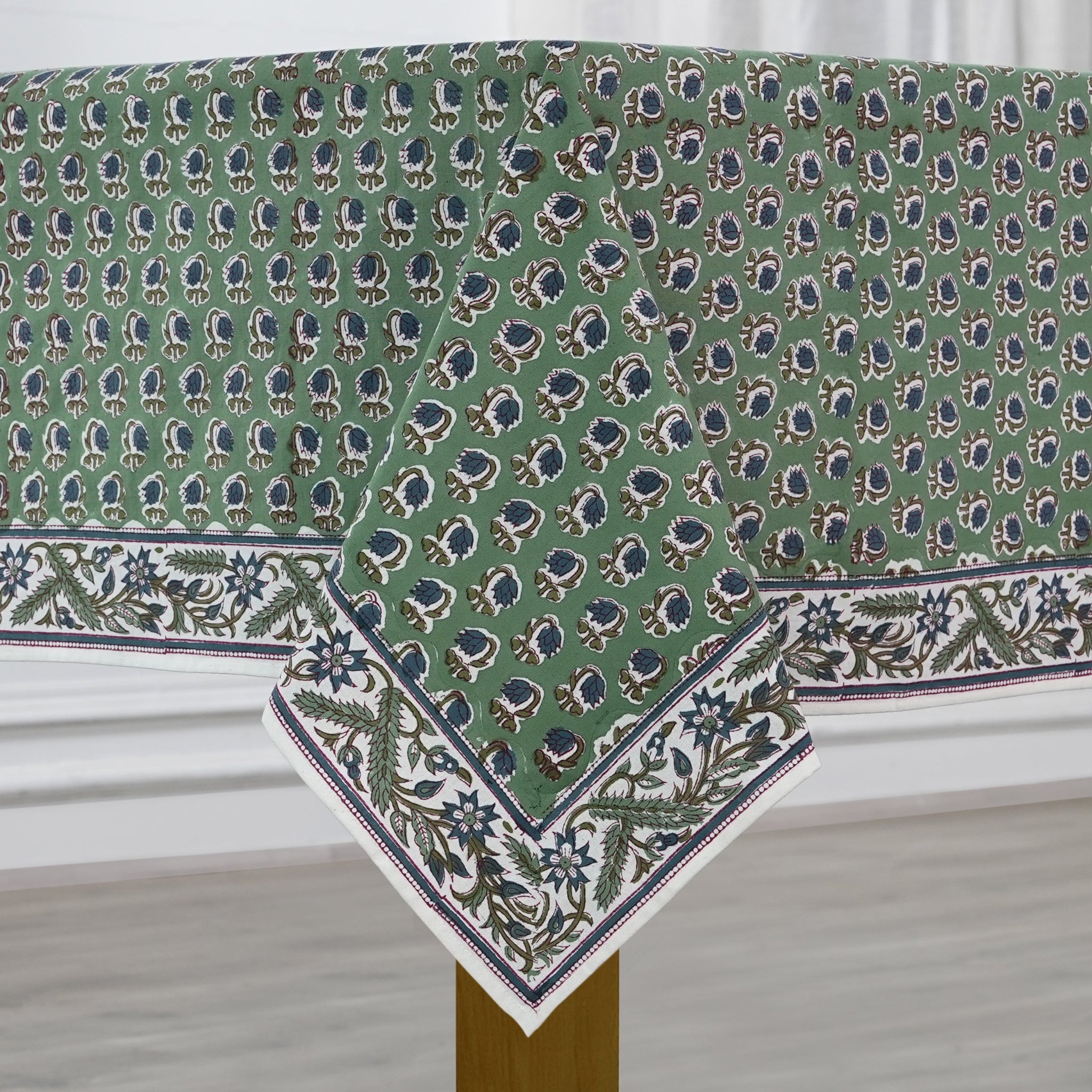 Green patterned tablecloth on a wooden table with a white curtain background