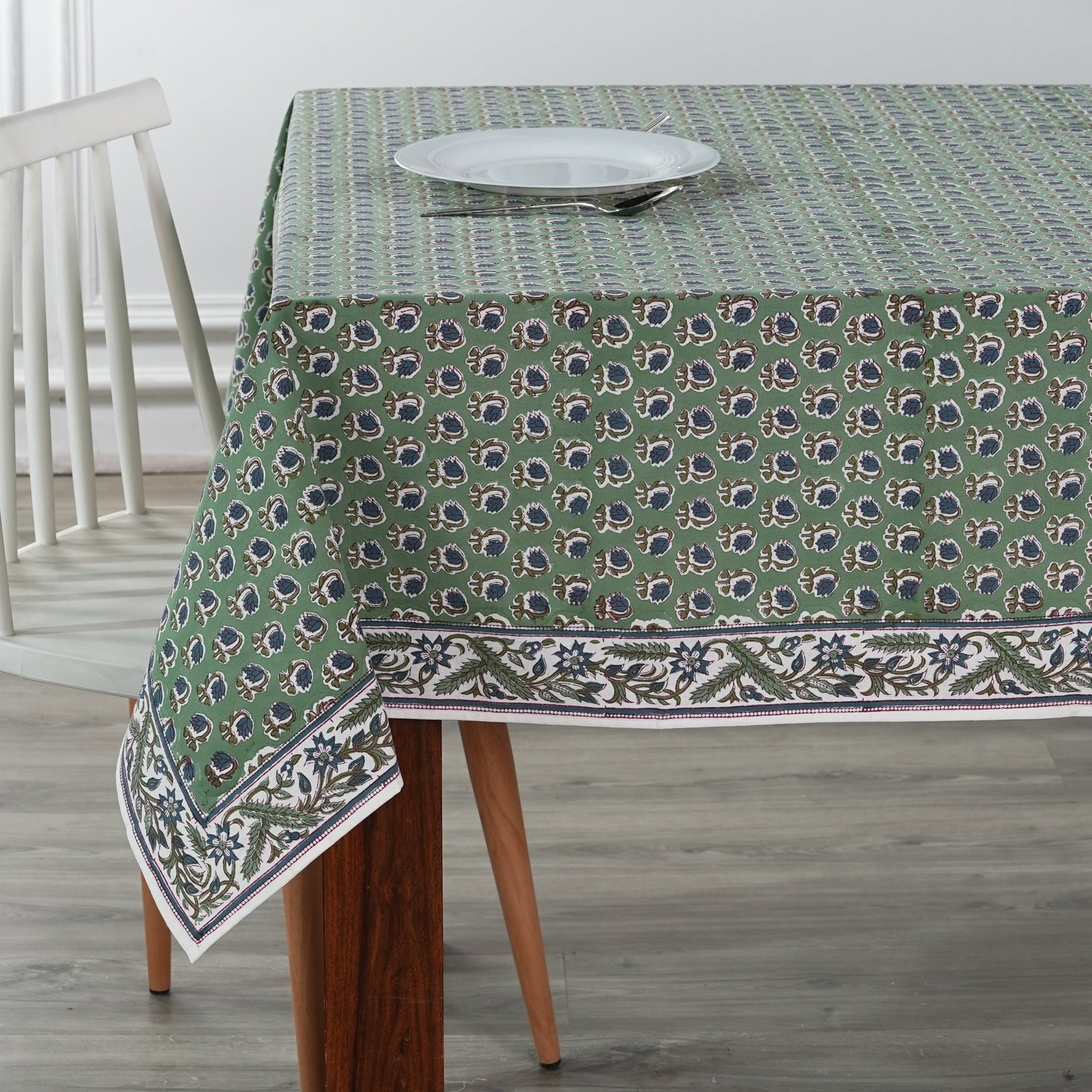 Green patterned tablecloth on a wooden table with a white chair in the background.