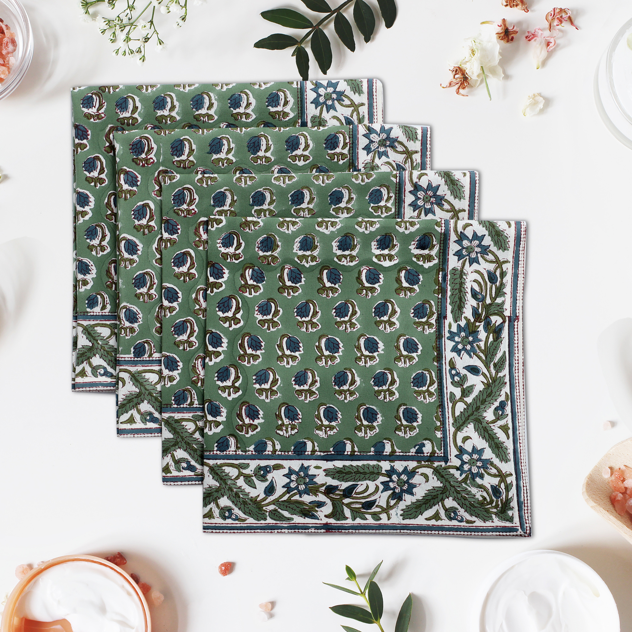 Set of green patterned napkins on a white surface with floral decorations.