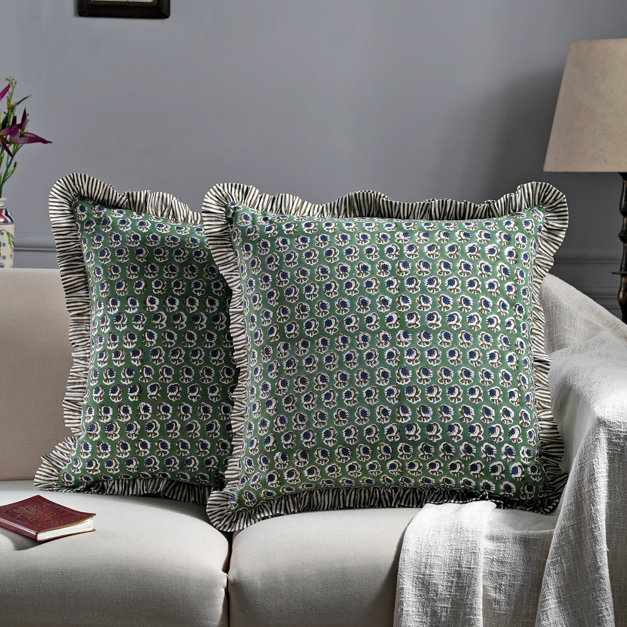 Two green patterned pillows on a beige sofa with a gray wall in the background.