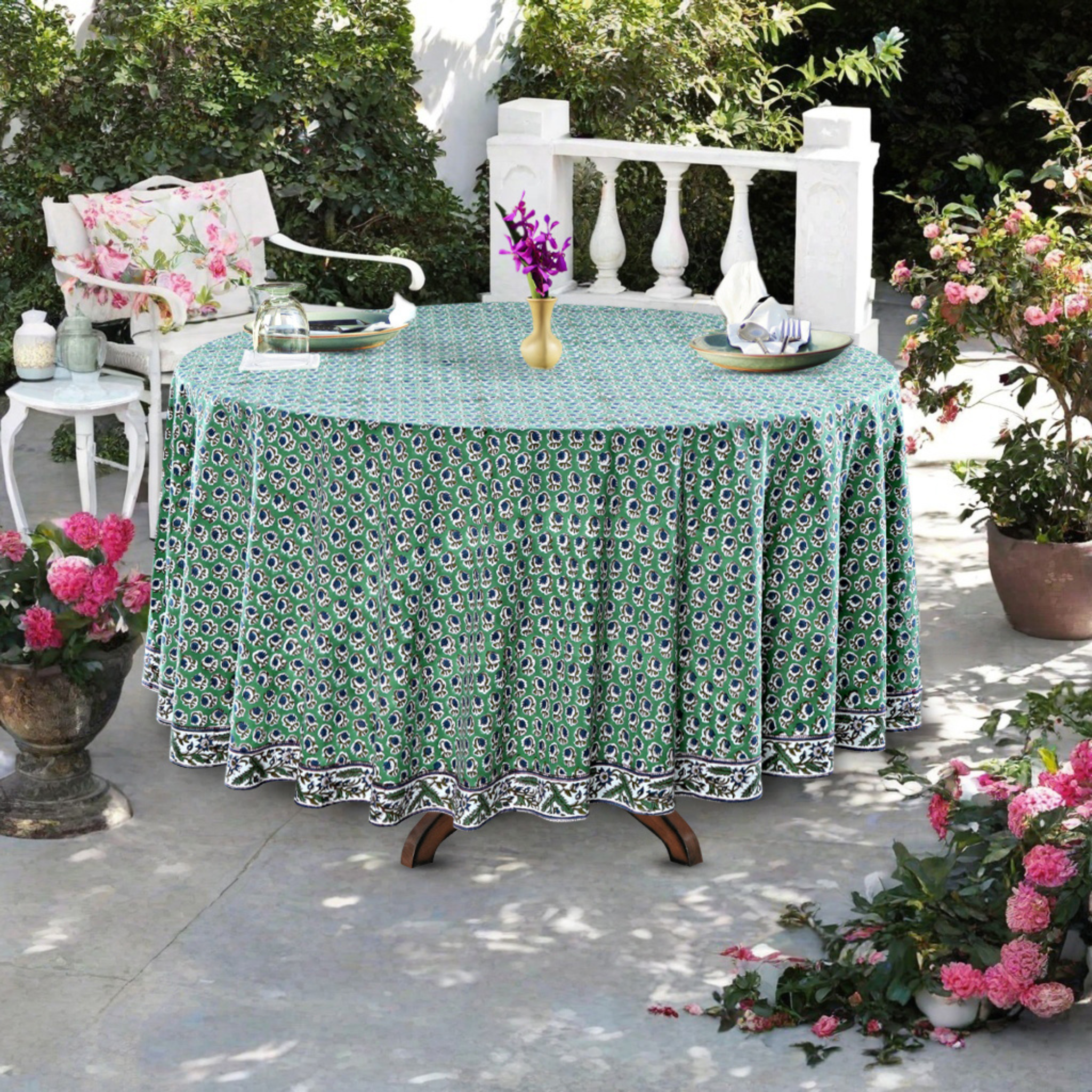 Outdoor table setting with a green floral tablecloth, surrounded by potted plants and chairs.