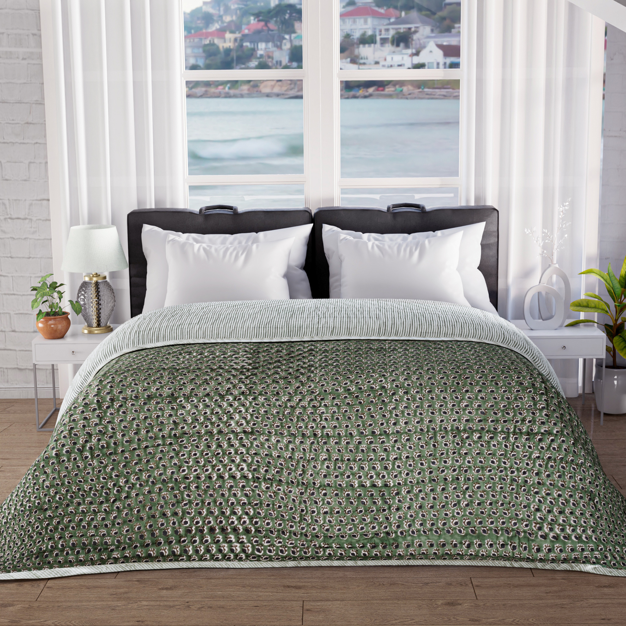 Bed with green patterned comforter in a room with large windows showing a waterfront view.
