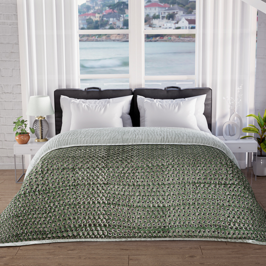 Bed with green patterned comforter in a room with large windows showing a waterfront view.