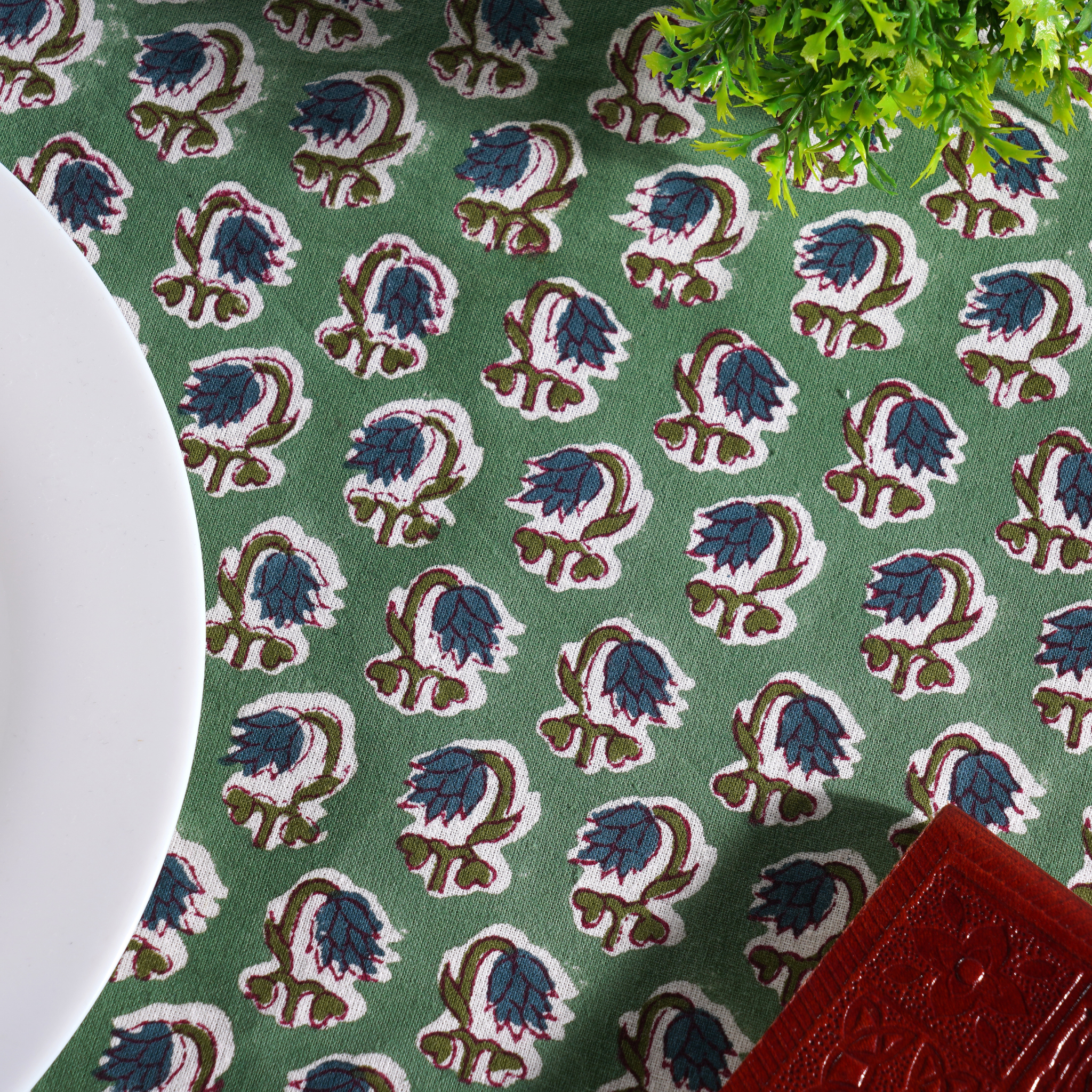 Green fabric with floral pattern and a white plate on a green surface