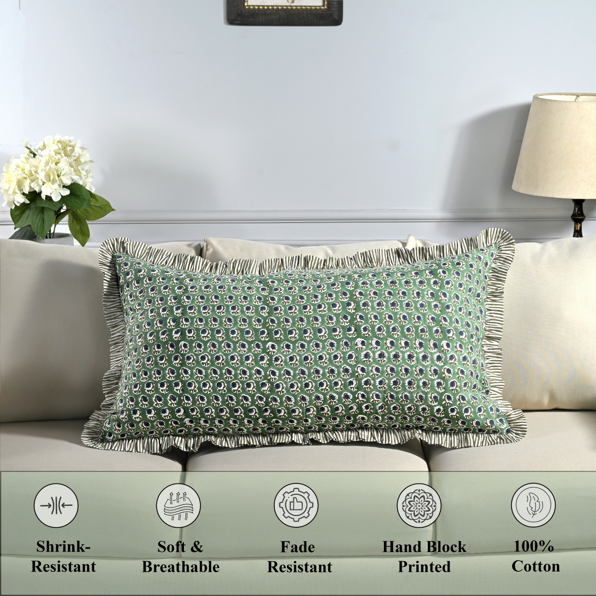 Cotton block print pillow cover placed on a bed with lamp and flowers in background.