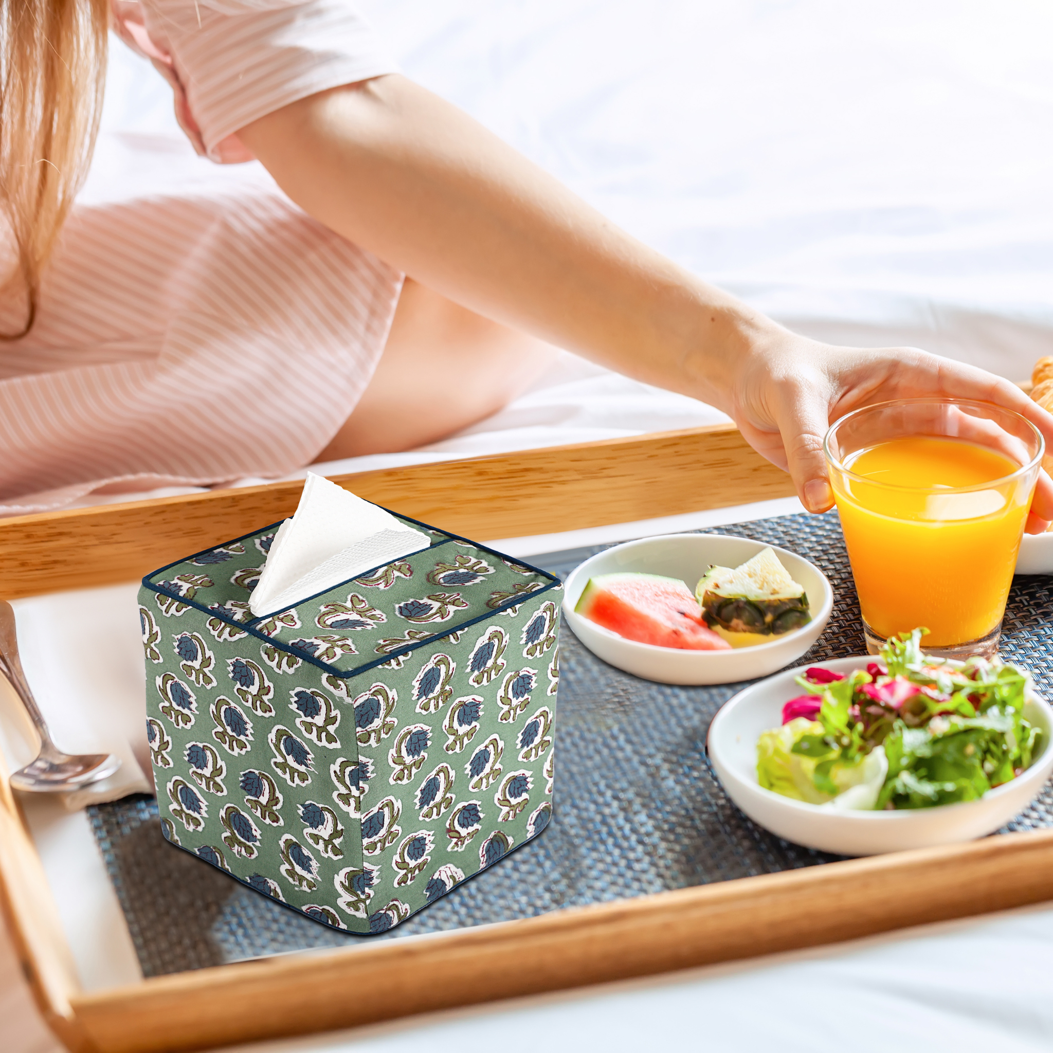 Person sitting on a bed with a tray of food and a tissue box.
