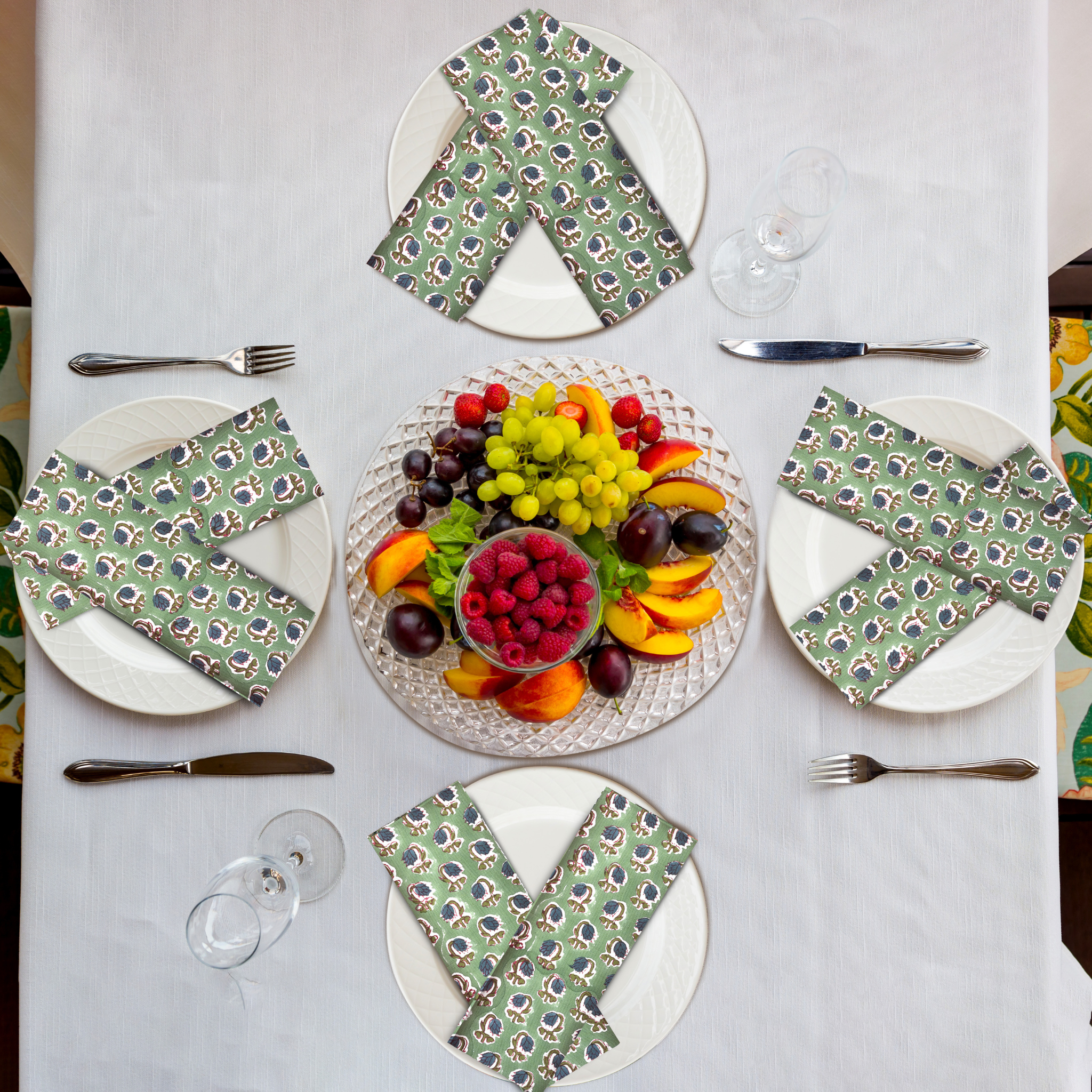 Table setting with plates, napkins, and a fruit platter on a white tablecloth.