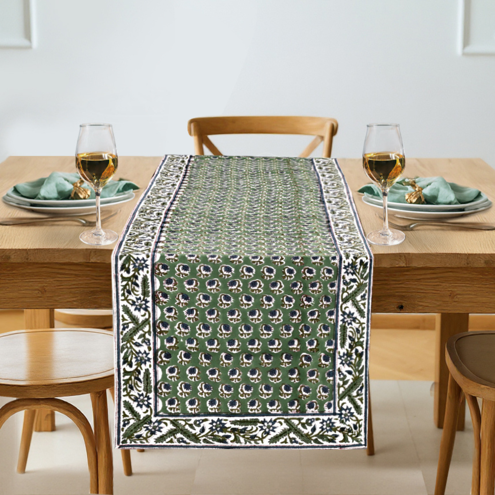 Dining table set with a green patterned table runner, glasses, and plates.