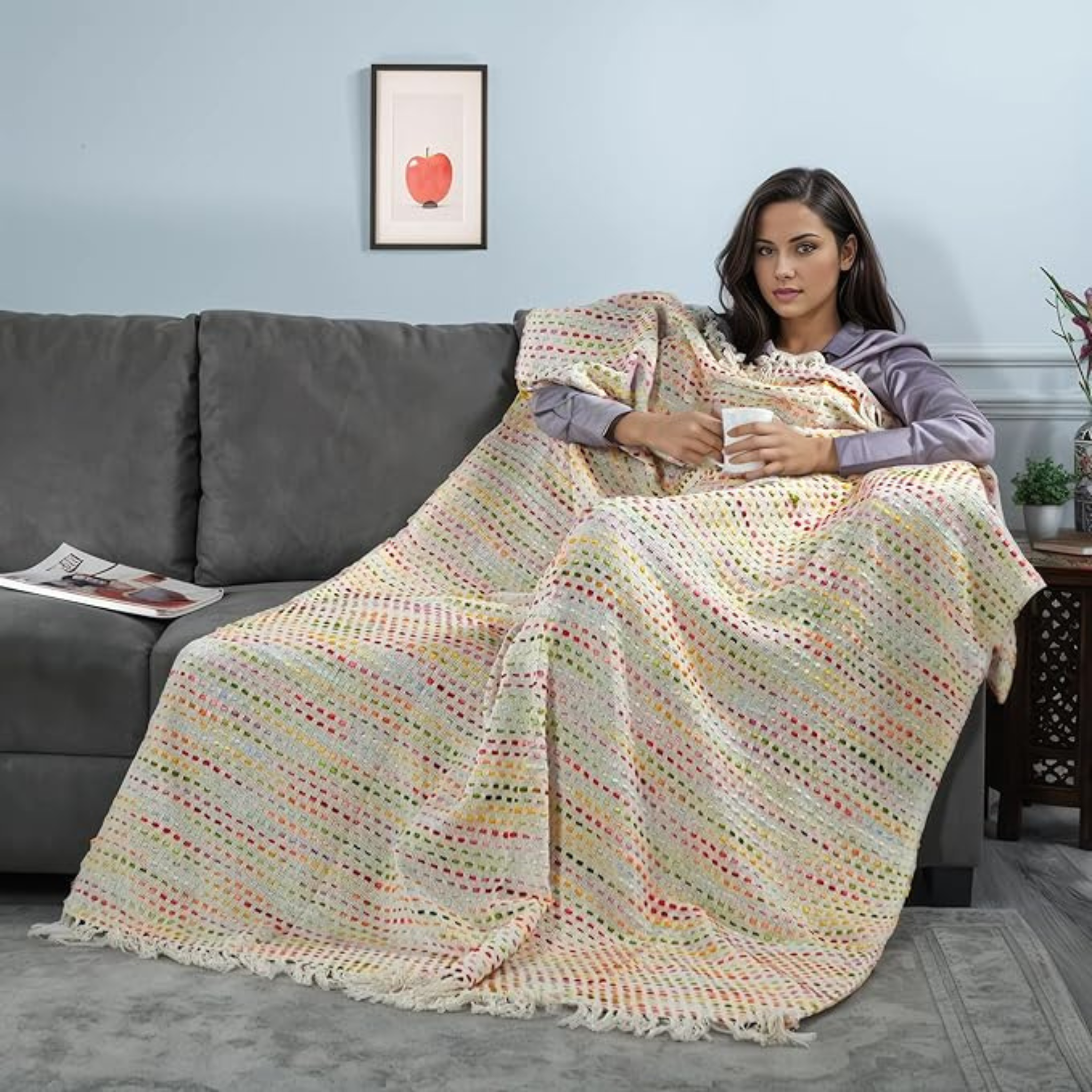 Woman sitting on a couch under a colorful blanket holding a mug.