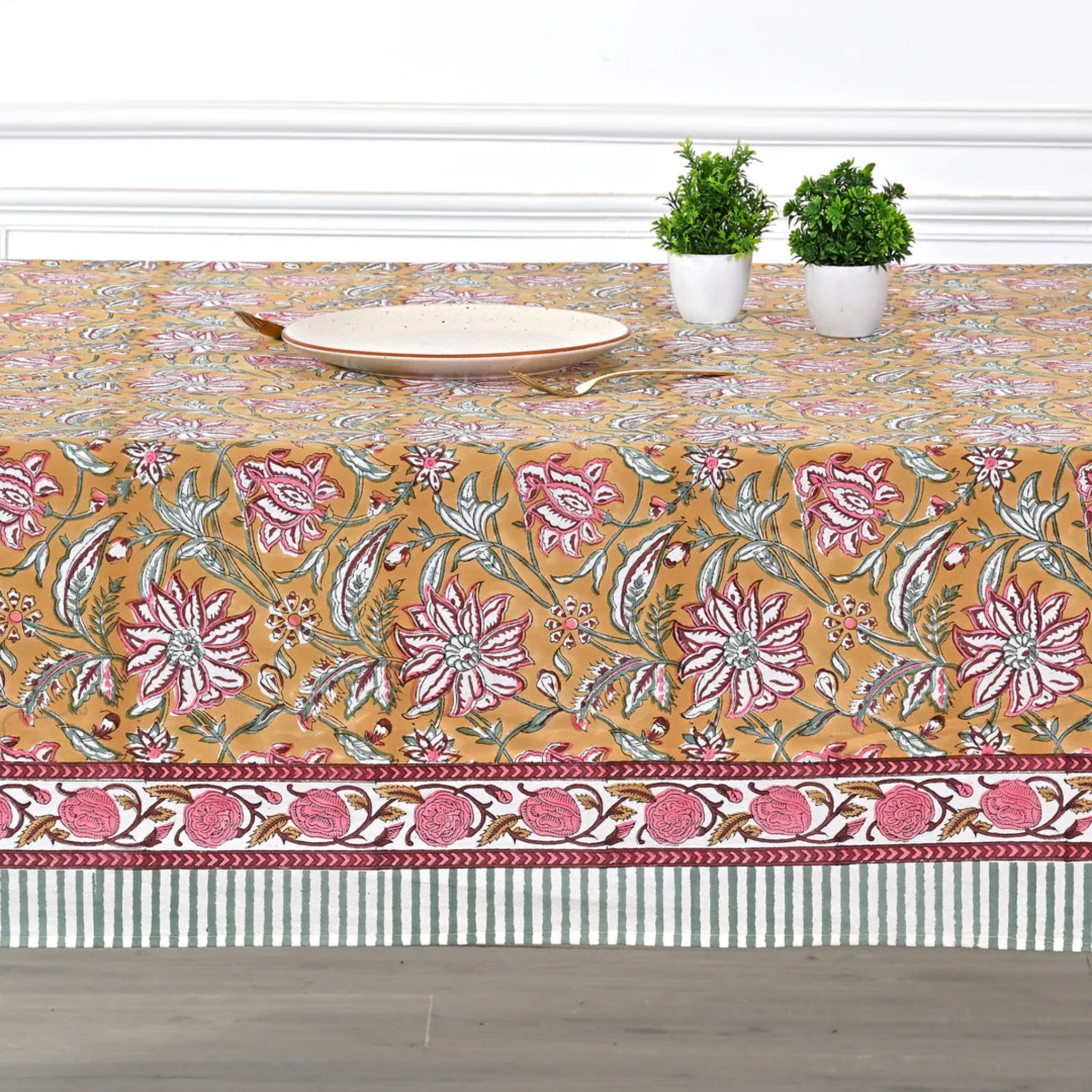 Floral patterned tablecloth on a wooden table with two potted plants.
