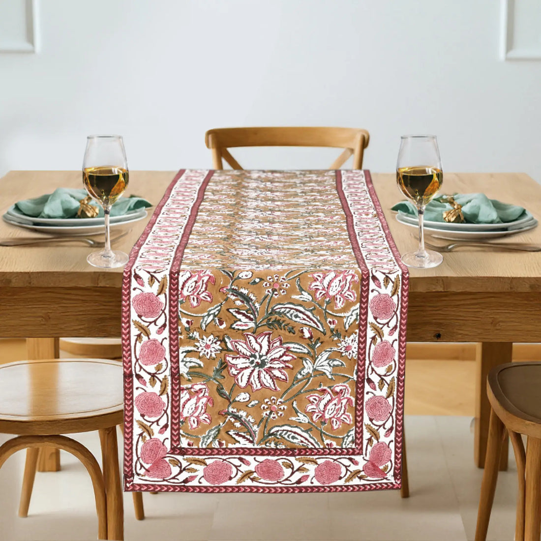 Dining table with a floral patterned table runner, glasses, and plates.