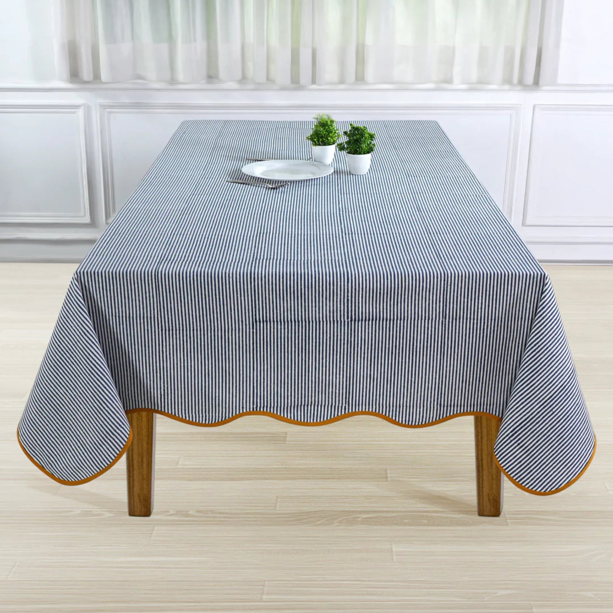 Tablecloth with blue and white stripes on a wooden table in a room with white walls and curtains.