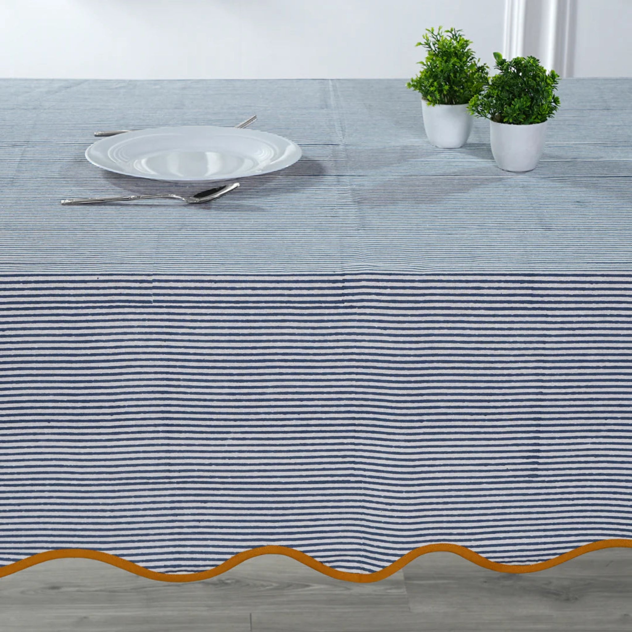 Tablecloth with blue and white stripes and gold border on a table setting.