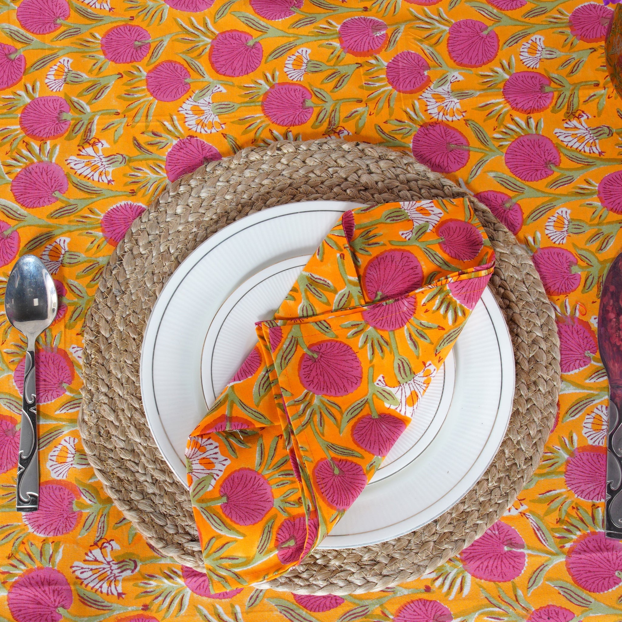 Table setting with a colorful tablecloth, plates, cutlery, and folded napkin.