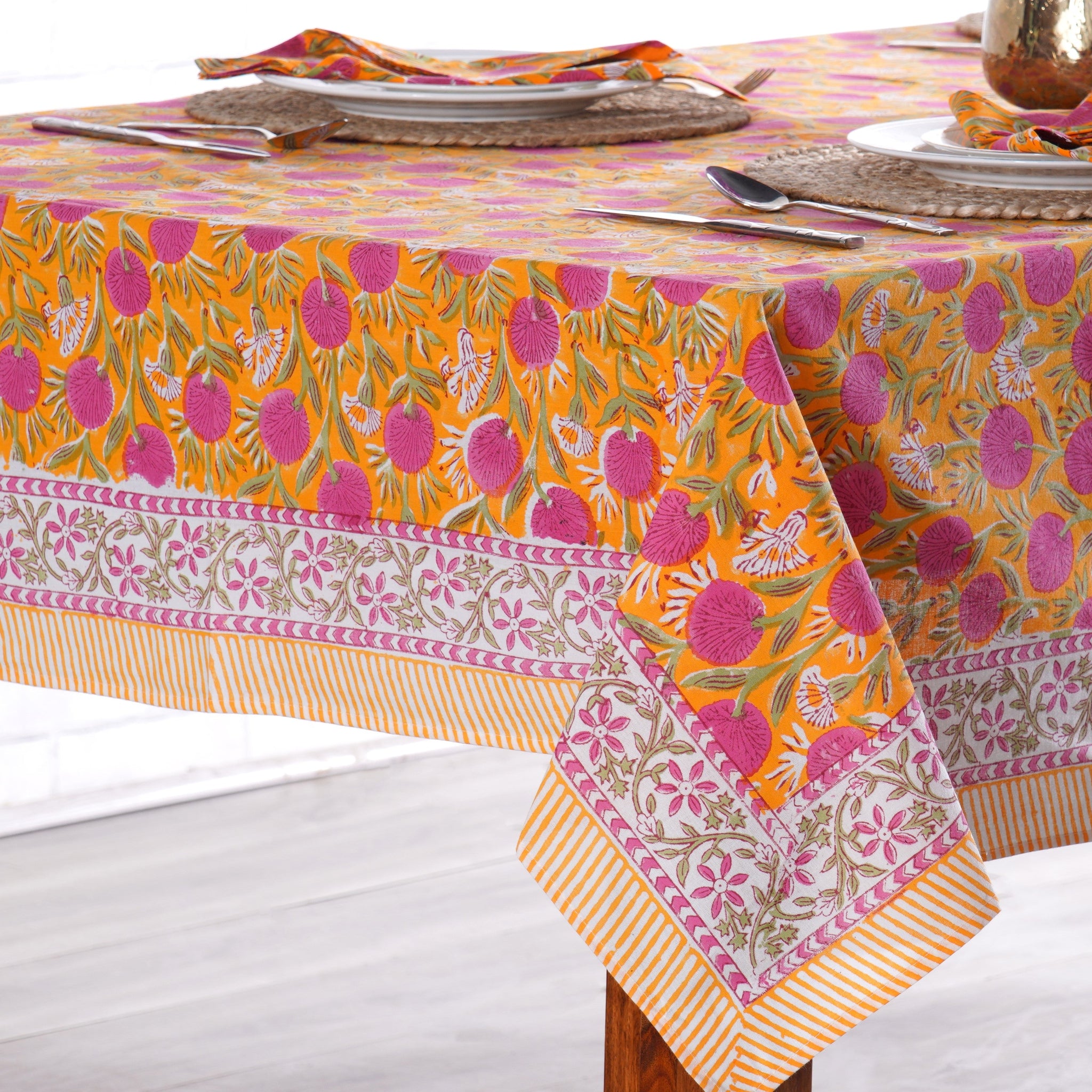 Colorful patterned tablecloth on a wooden table with plates and cutlery.